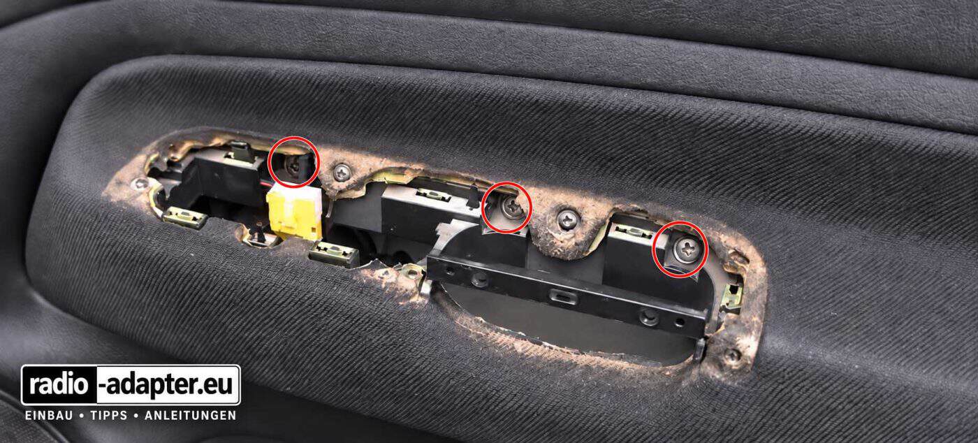 VW Golf IV (1999–2005): Fahrertür mit entferntem Fensterheber-Bedienteil und drei rot markierten Befestigungsschrauben unter der Griffmulde.